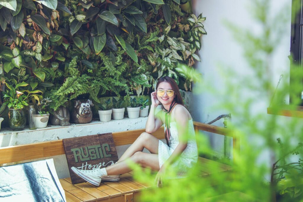Young woman smiling and posing in a lush, vibrant garden setting with rustic charm.